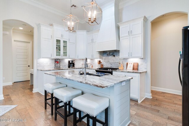 kitchen with light wood-type flooring, premium range hood, white cabinets, and a kitchen island with sink