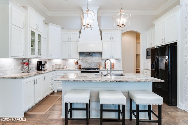 kitchen with hardwood / wood-style floors, stainless steel appliances, white cabinetry, a kitchen bar, and a kitchen island with sink