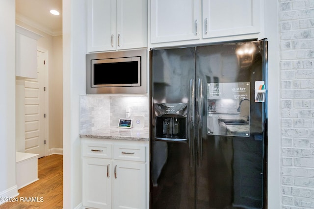 kitchen featuring crown molding, light stone counters, light hardwood / wood-style floors, white cabinetry, and black refrigerator with ice dispenser