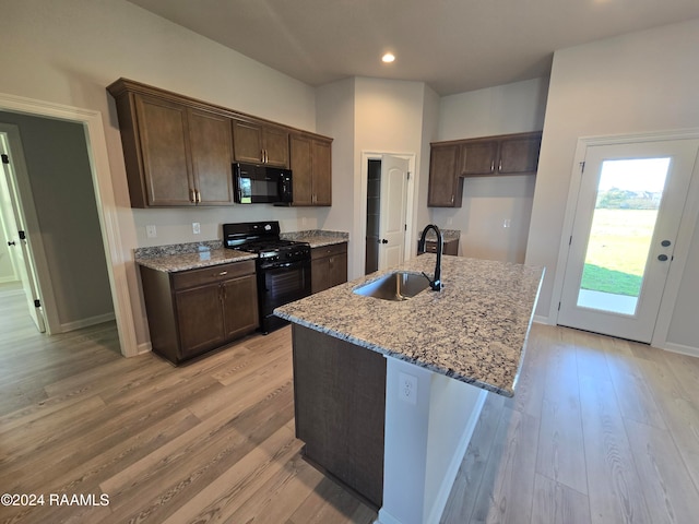 kitchen featuring sink, light stone counters, a kitchen island with sink, black appliances, and light wood-type flooring