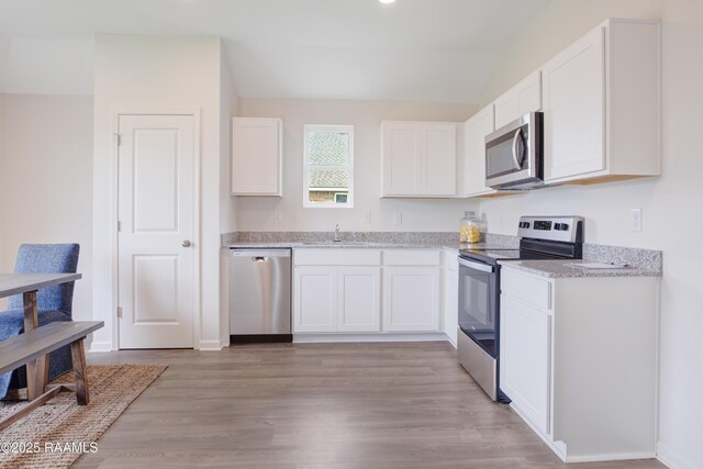 kitchen featuring lofted ceiling, stainless steel appliances, a sink, light wood-style floors, and white cabinets