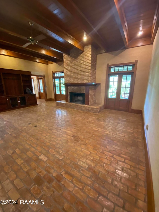 unfurnished living room featuring ceiling fan, beamed ceiling, a brick fireplace, and wooden ceiling