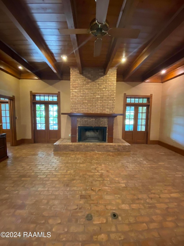 unfurnished living room with wood ceiling, beamed ceiling, a fireplace, ceiling fan, and french doors