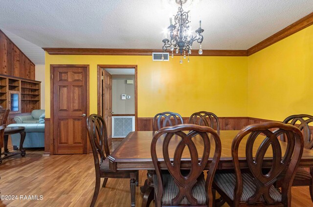 dining room featuring light hardwood / wood-style flooring, wood walls, a textured ceiling, and an inviting chandelier