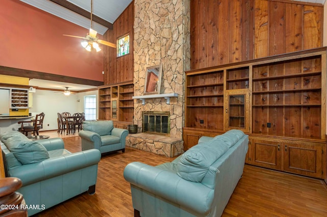 living room with ceiling fan, a stone fireplace, hardwood / wood-style floors, and high vaulted ceiling