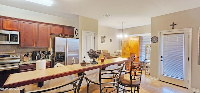 kitchen featuring pendant lighting, tasteful backsplash, an inviting chandelier, appliances with stainless steel finishes, and light tile patterned floors