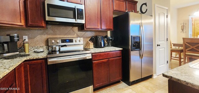 kitchen with light stone countertops, appliances with stainless steel finishes, light tile patterned floors, and decorative backsplash