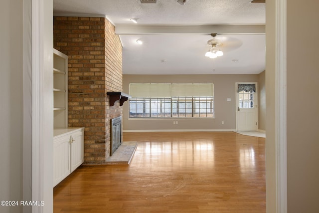 unfurnished living room featuring a brick fireplace, ceiling fan, light wood-type flooring, and a textured ceiling