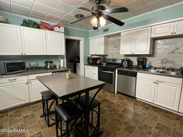 kitchen with ceiling fan, sink, white cabinetry, stainless steel appliances, and a drop ceiling