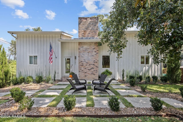 rear view of property featuring board and batten siding, a chimney, brick siding, and a patio