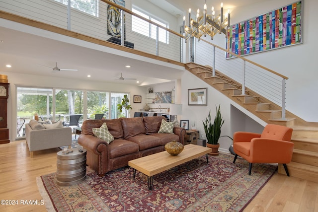 living area featuring light wood-type flooring, a towering ceiling, recessed lighting, ceiling fan with notable chandelier, and stairway