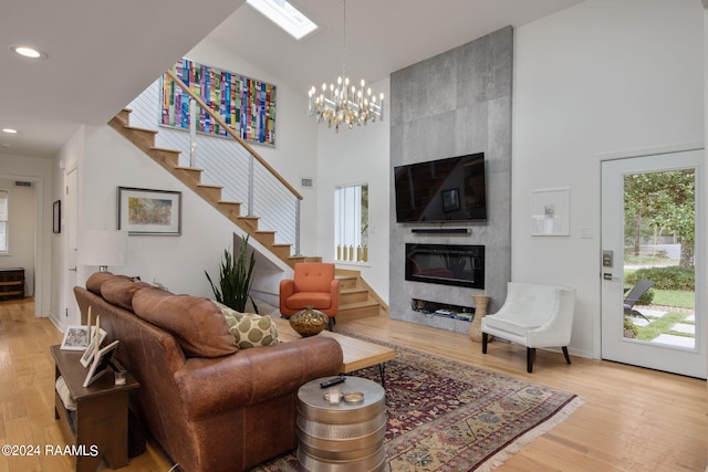 living room with a skylight, an inviting chandelier, hardwood / wood-style floors, a fireplace, and high vaulted ceiling