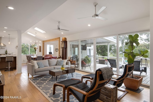 living room with lofted ceiling, ceiling fan with notable chandelier, light wood-type flooring, and a healthy amount of sunlight