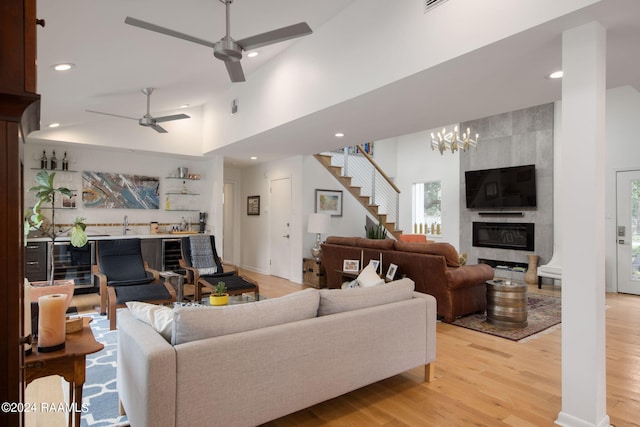 living room featuring a towering ceiling, ceiling fan with notable chandelier, beverage cooler, and light wood-type flooring