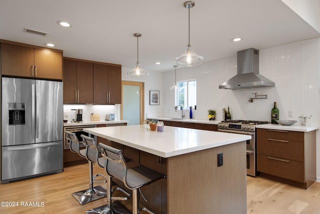 kitchen with a kitchen island, stainless steel appliances, wall chimney range hood, and light hardwood / wood-style flooring