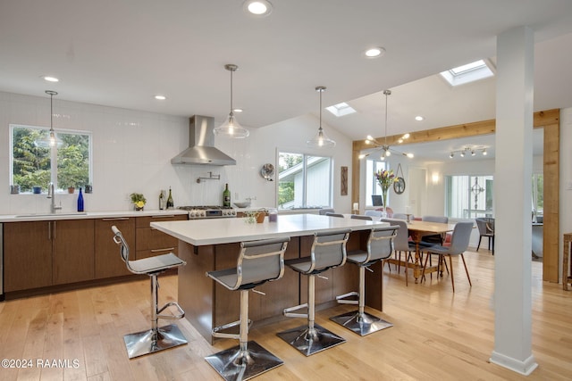 kitchen featuring sink, wall chimney range hood, light hardwood / wood-style flooring, and lofted ceiling with skylight