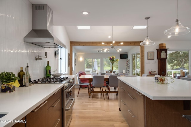 kitchen with a kitchen island, decorative light fixtures, light hardwood / wood-style flooring, wall chimney range hood, and stainless steel stove