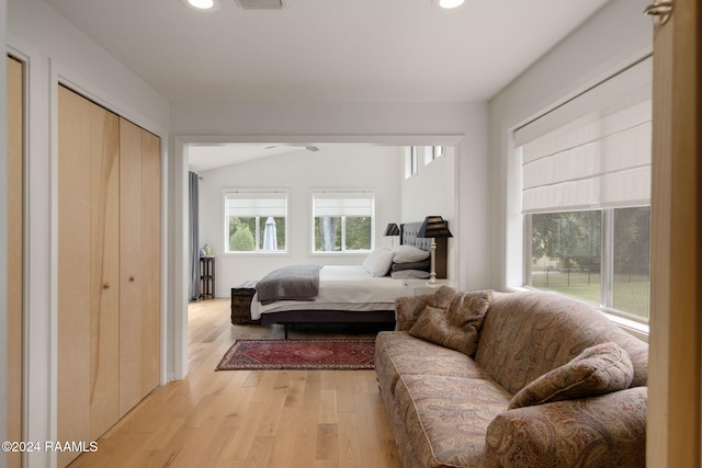 bedroom featuring light wood-type flooring, vaulted ceiling, and a closet