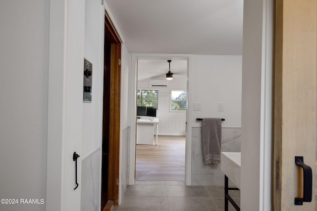 corridor with light hardwood / wood-style floors, vaulted ceiling, and a wall unit AC