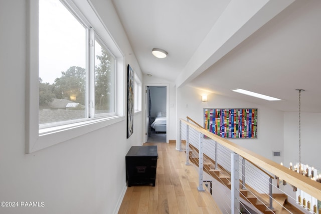 corridor featuring light wood-style floors, visible vents, baseboards, and an upstairs landing