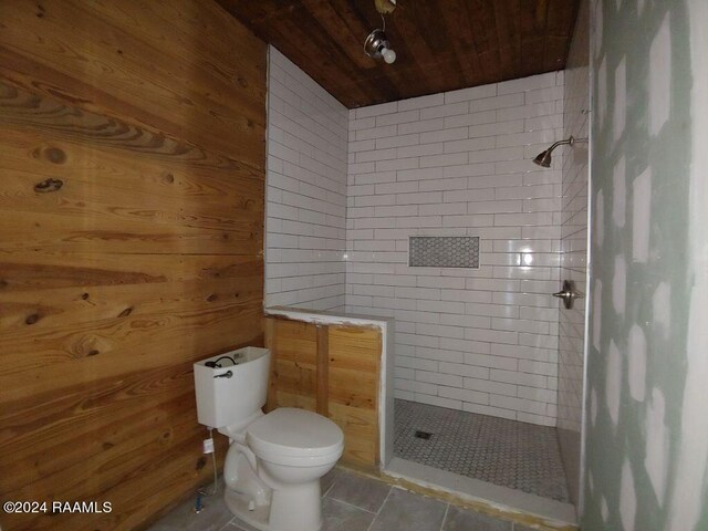 bathroom featuring wooden ceiling, a tile shower, wooden walls, toilet, and tile patterned floors