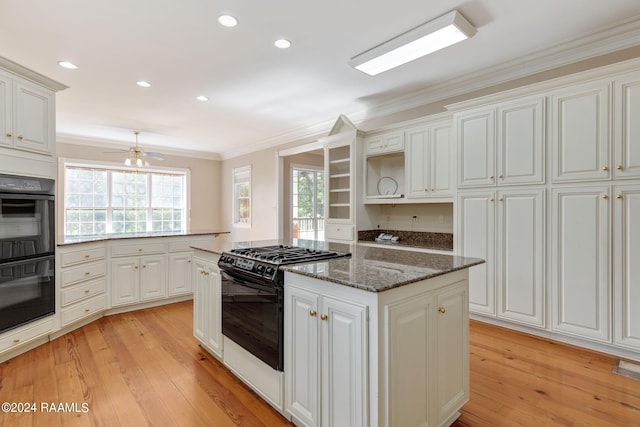 kitchen with gas range oven, light hardwood / wood-style flooring, black double oven, crown molding, and dark stone countertops