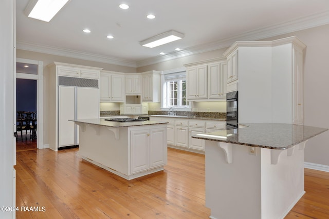 kitchen featuring dark stone countertops, a breakfast bar area, paneled built in fridge, and light hardwood / wood-style flooring