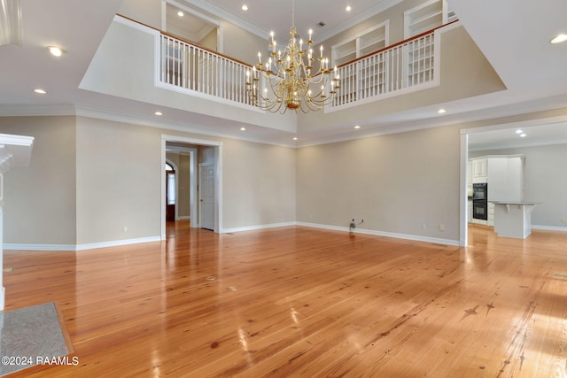 spare room featuring a notable chandelier, light wood-type flooring, ornamental molding, and a high ceiling