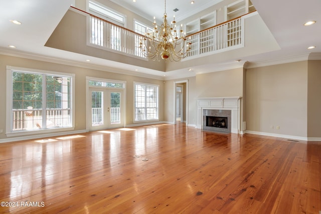 unfurnished living room with light hardwood / wood-style floors, a towering ceiling, a fireplace, crown molding, and a notable chandelier