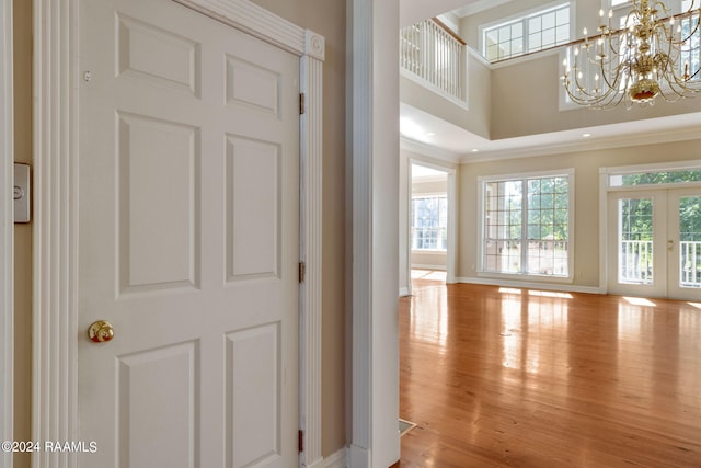 entrance foyer featuring french doors, light hardwood / wood-style flooring, a high ceiling, a notable chandelier, and crown molding