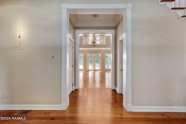 hallway with light wood-type flooring, electric panel, an inviting chandelier, crown molding, and french doors