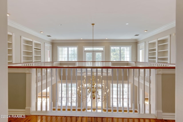 corridor featuring wood-type flooring, ornamental molding, built in features, and a chandelier