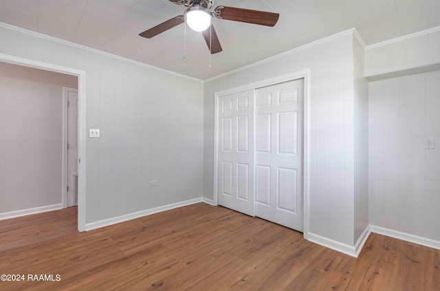 unfurnished bedroom featuring a closet, hardwood / wood-style flooring, wood walls, crown molding, and ceiling fan