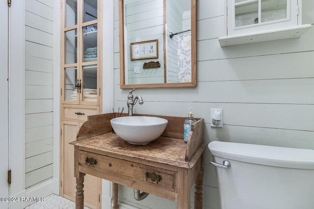 bathroom featuring wood walls, walk in shower, sink, and toilet