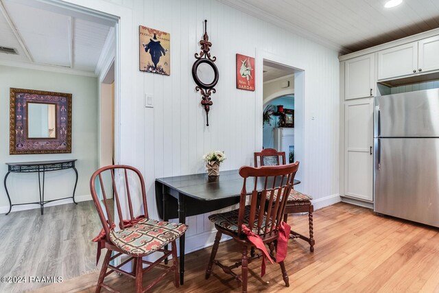 dining area featuring crown molding, wood walls, and light hardwood / wood-style flooring