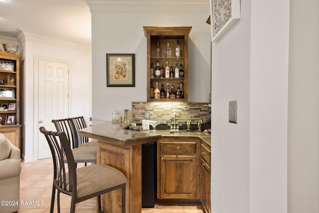 bar featuring dark stone counters, crown molding, decorative backsplash, and light tile patterned floors