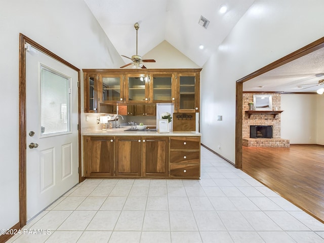 kitchen featuring vaulted ceiling, kitchen peninsula, light hardwood / wood-style flooring, a brick fireplace, and ceiling fan