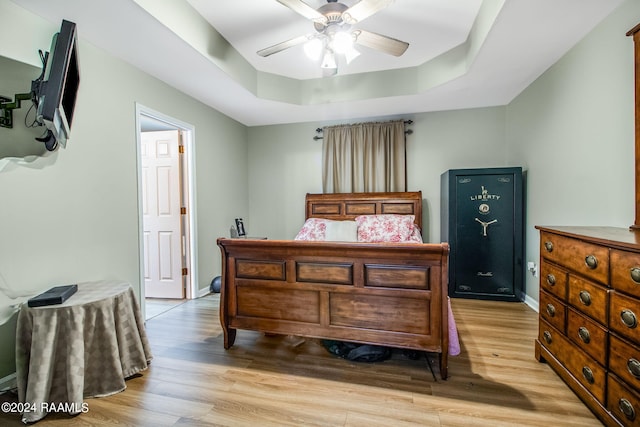 bedroom featuring a raised ceiling, ceiling fan, and light wood-type flooring