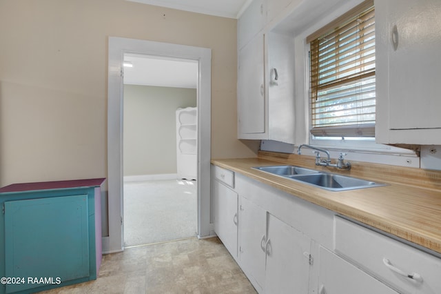 kitchen with white cabinetry, crown molding, and sink