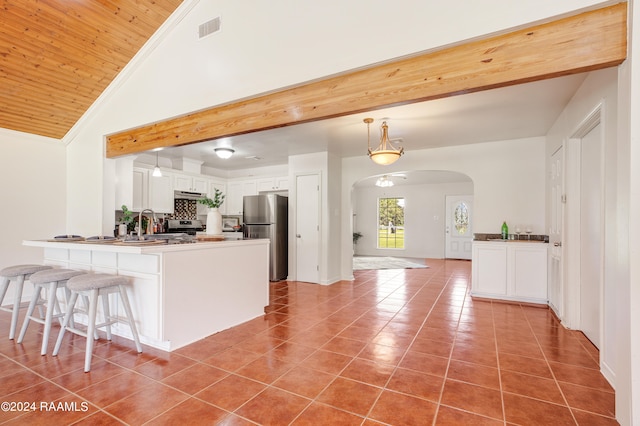 kitchen featuring white cabinets, stainless steel fridge, light tile patterned floors, kitchen peninsula, and a breakfast bar