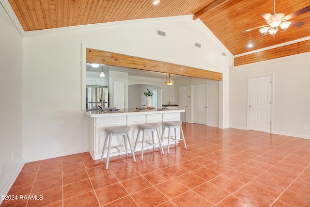 kitchen with ceiling fan, beamed ceiling, wood ceiling, stainless steel fridge, and a breakfast bar