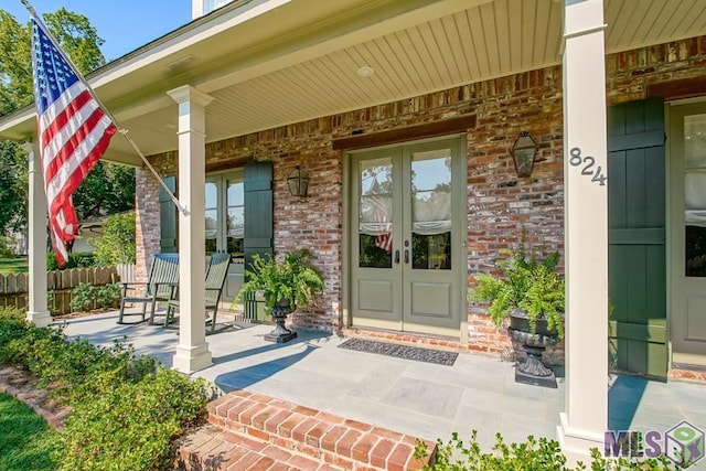 entrance to property with covered porch, french doors, fence, and brick siding