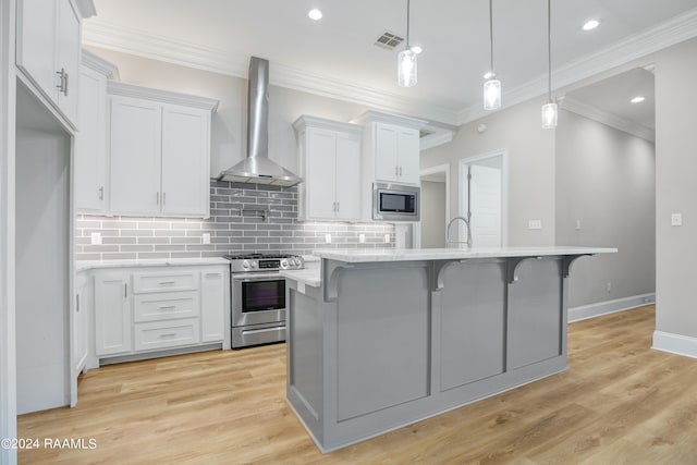 kitchen with wall chimney exhaust hood, white cabinets, appliances with stainless steel finishes, and light wood-type flooring