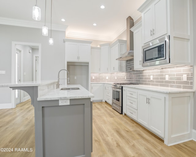 kitchen featuring appliances with stainless steel finishes, white cabinets, wall chimney exhaust hood, a kitchen island with sink, and sink