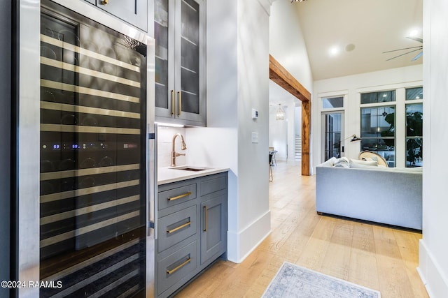 kitchen featuring decorative backsplash, light wood-type flooring, lofted ceiling, beverage cooler, and sink