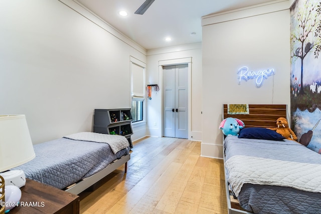 bedroom with crown molding, light hardwood / wood-style floors, ceiling fan, and a closet