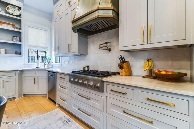 kitchen with light stone counters, tasteful backsplash, stainless steel appliances, light hardwood / wood-style flooring, and premium range hood