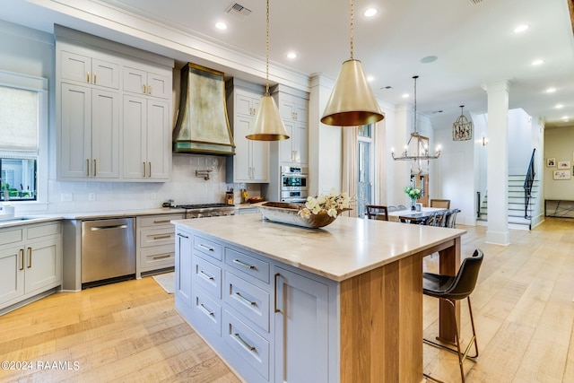 kitchen with light hardwood / wood-style floors, pendant lighting, stainless steel appliances, a center island, and custom exhaust hood