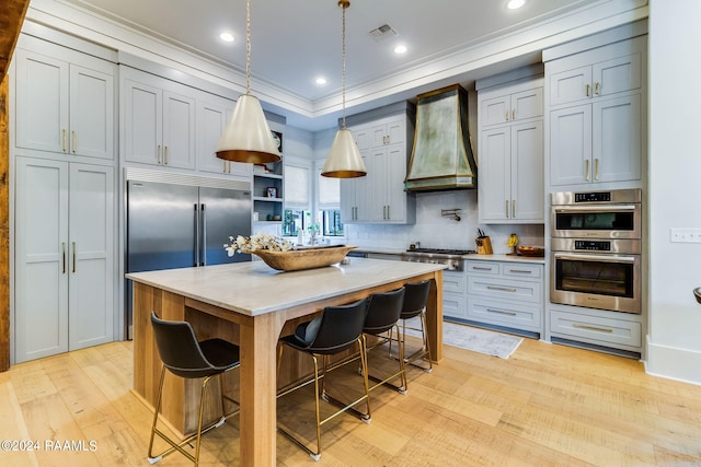 kitchen featuring premium range hood, light wood-type flooring, decorative light fixtures, a center island, and light stone countertops