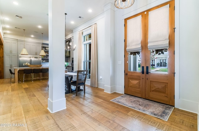 entrance foyer with ornamental molding, an inviting chandelier, and light hardwood / wood-style floors